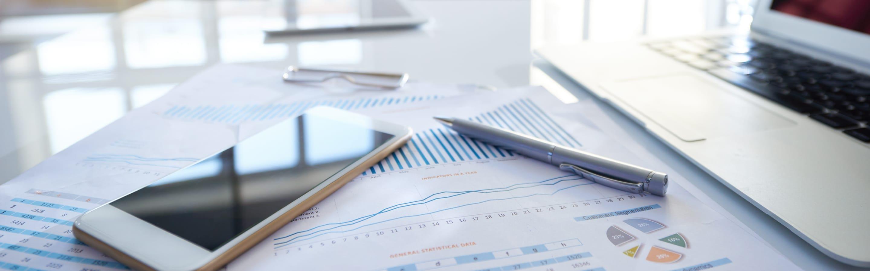 Focus image of a smart phone on top of a financial report and a laptop in the background 