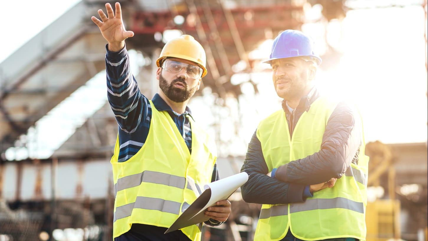 Two male construction workers talking outside 