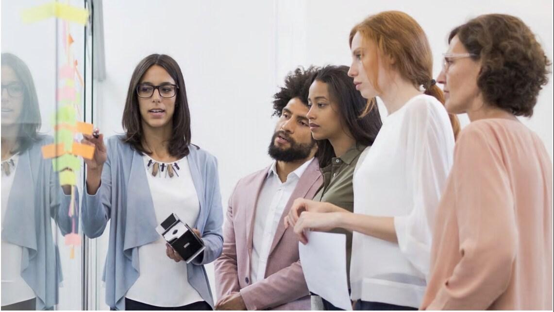 Five employees surrounding a white board talking in an pen place